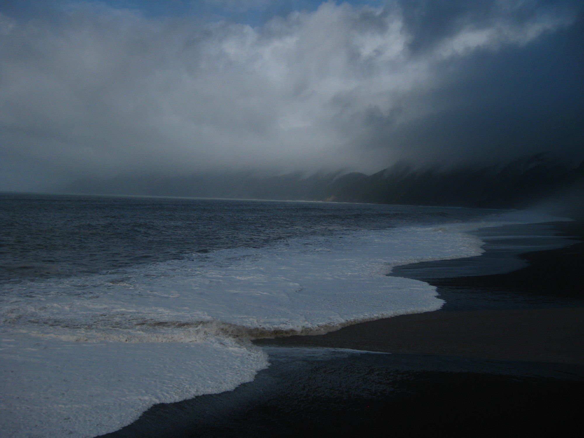 Surf running up a dark beach on the Lost Coast under low cloud