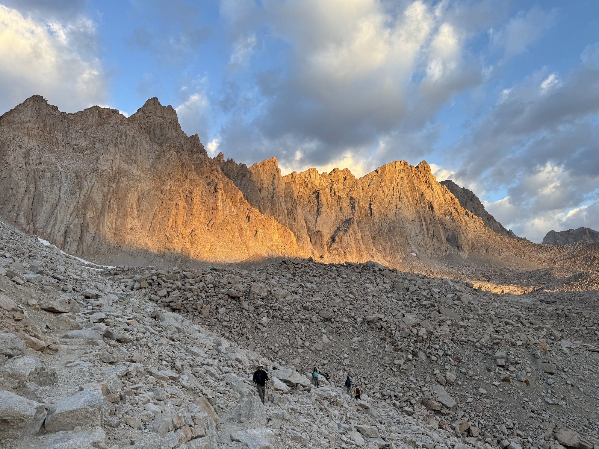 Jagged granite walls lit orange by alpenglow above a wide field of talus