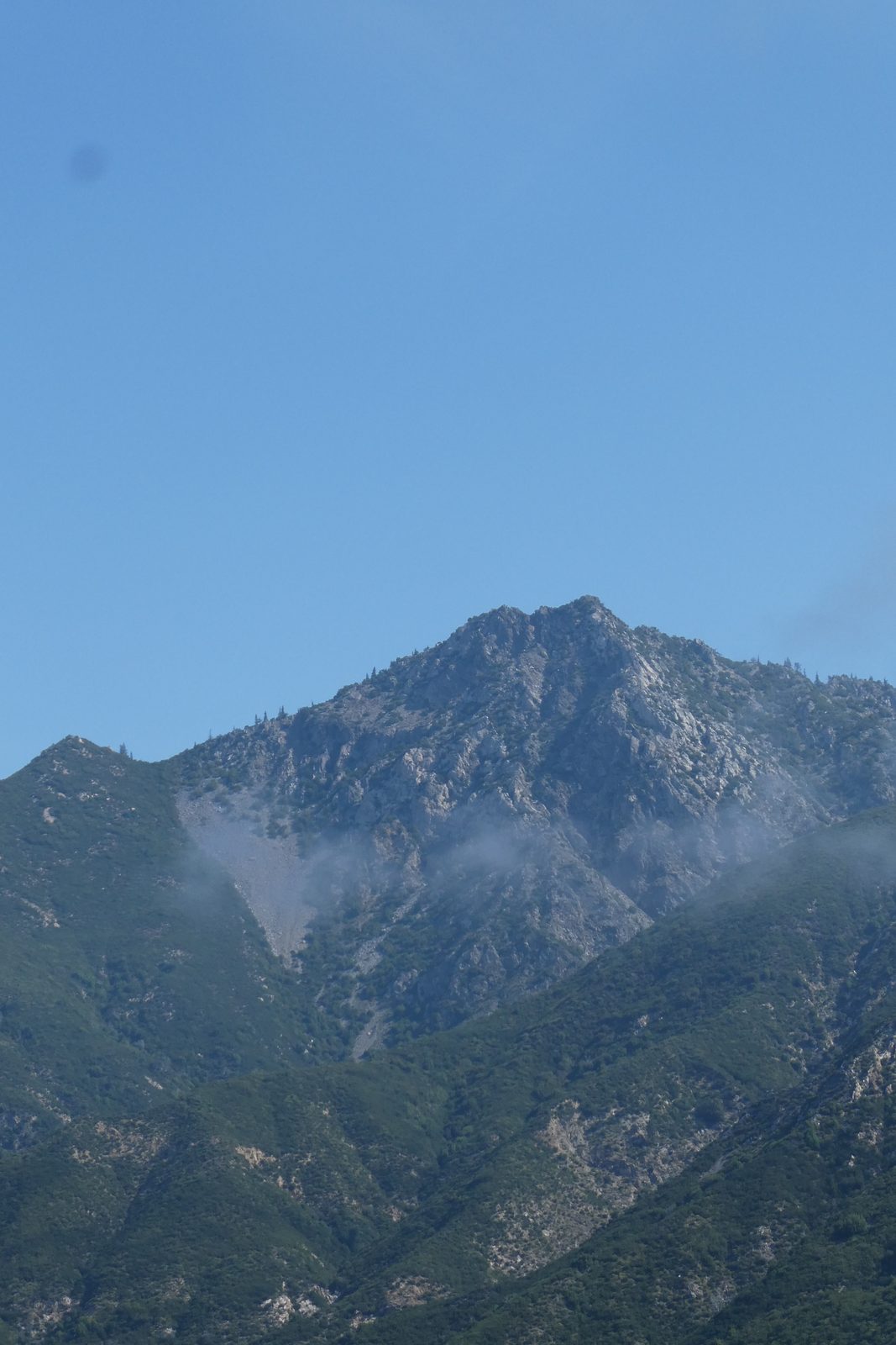 Rocky mountain summit with wisps of fog under a blue sky
