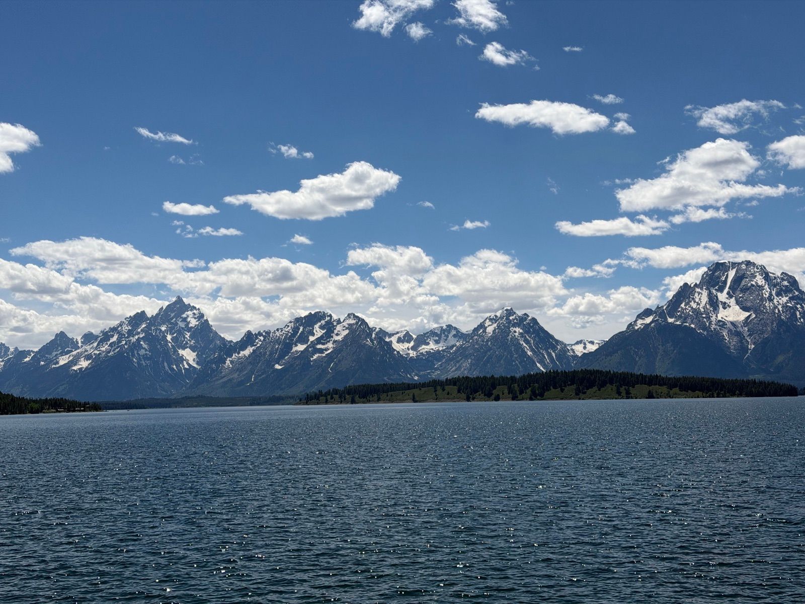 Snow-streaked Teton Range rising across a wide blue alpine lake