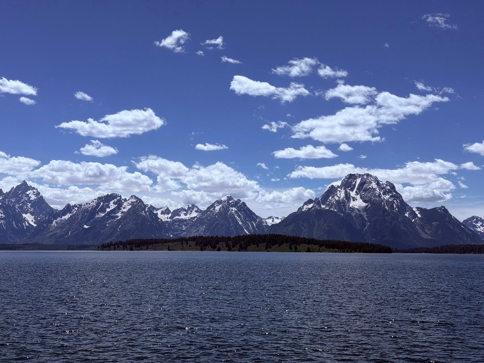 Jagged Teton peaks above a calm lake and forested shoreline