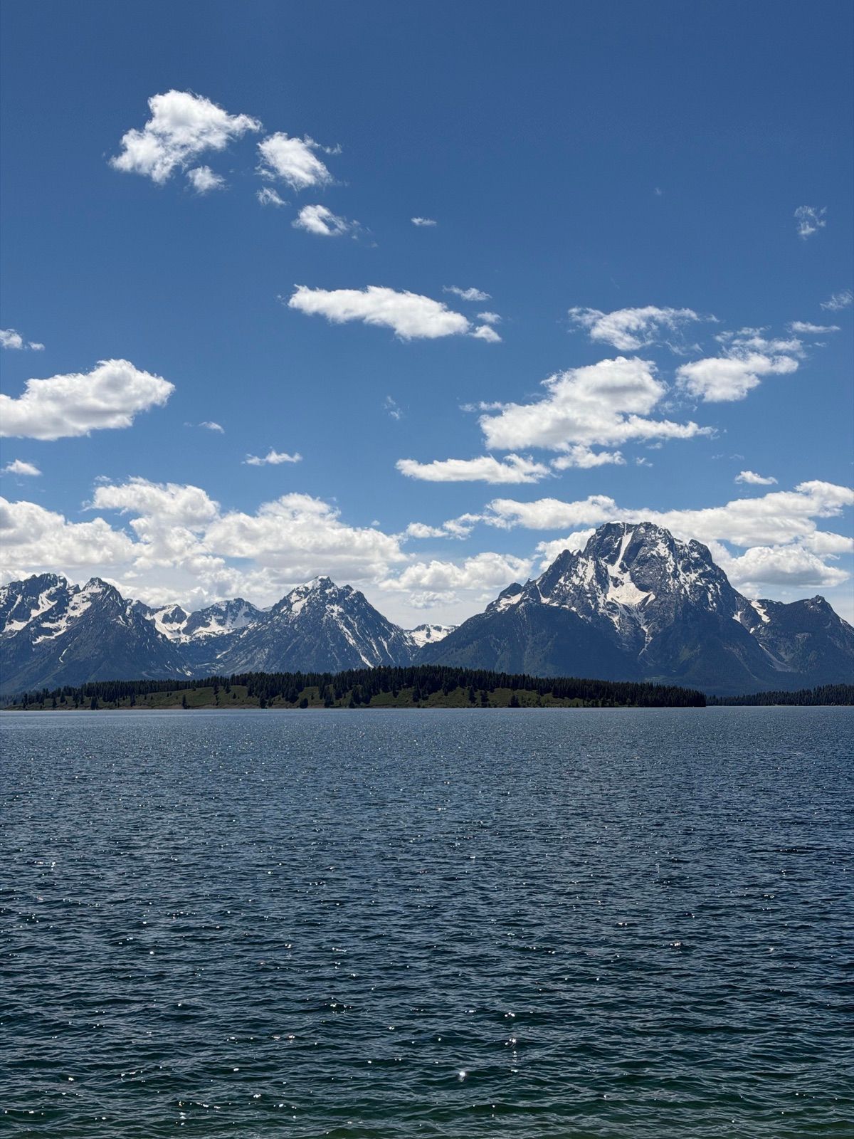Teton peaks and forest reflected across a still blue lake