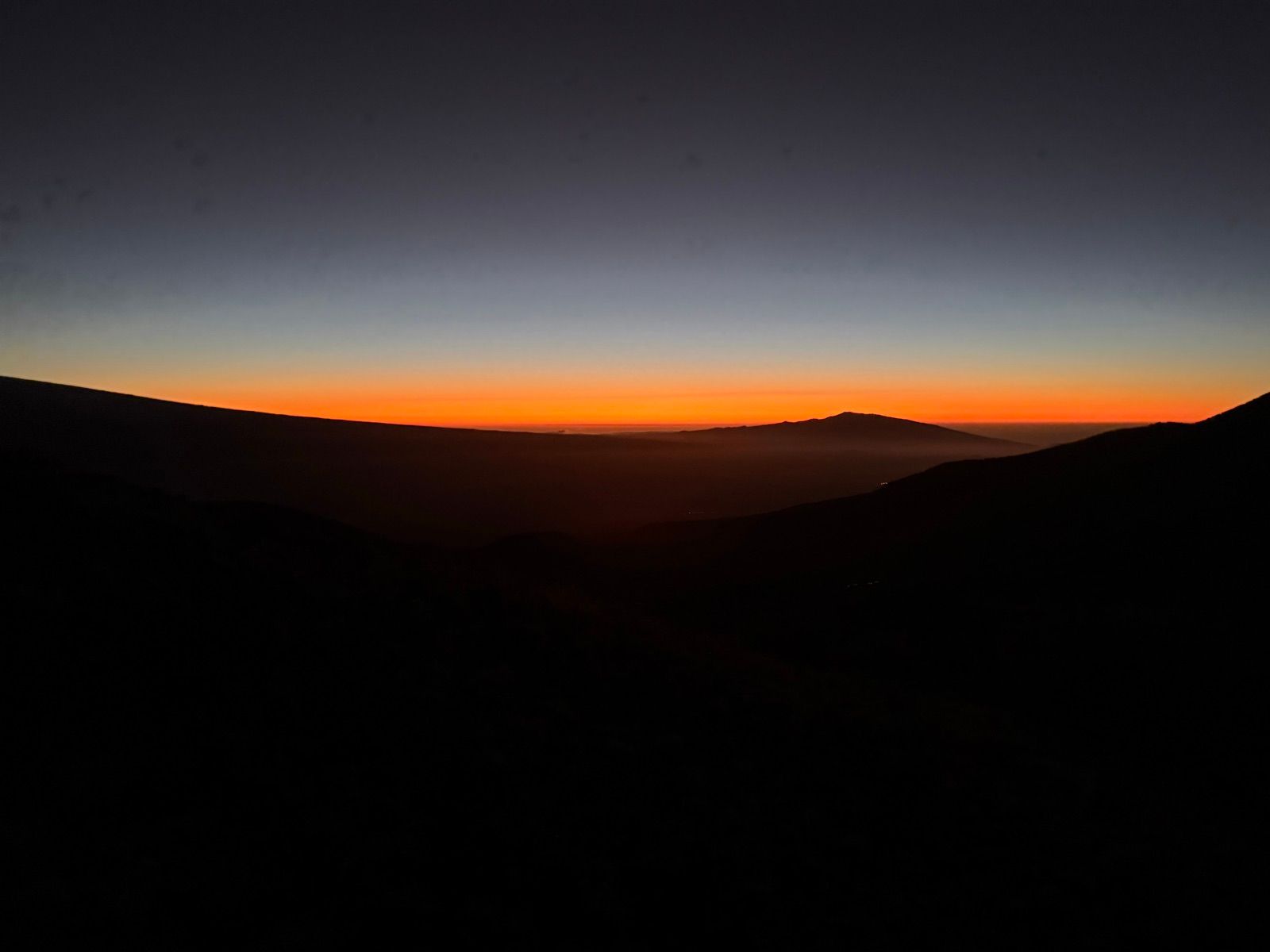 Volcanic ridges silhouetted beneath an orange twilight sky