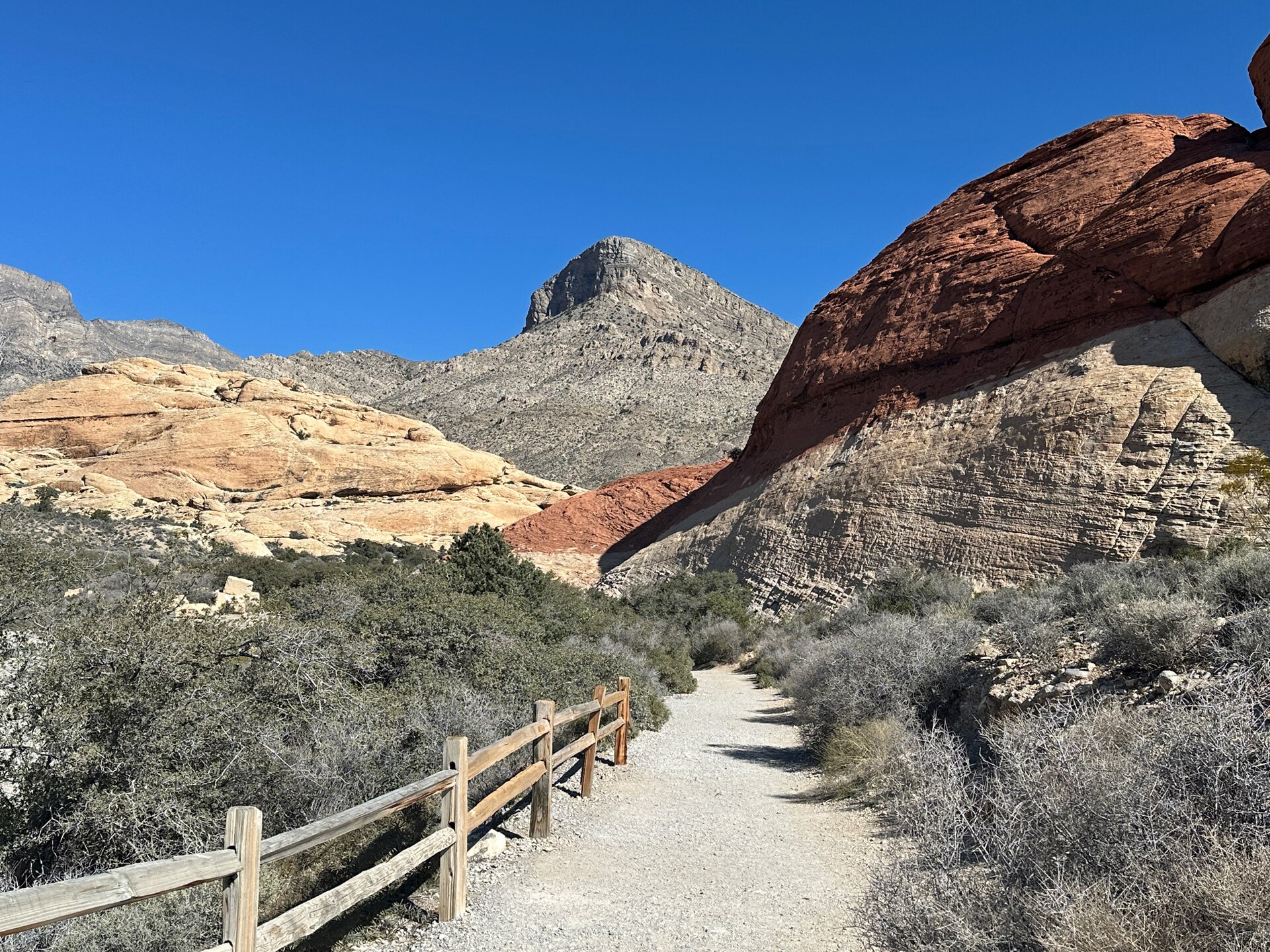 Gravel trail and wooden fence leading toward layered red and tan sandstone