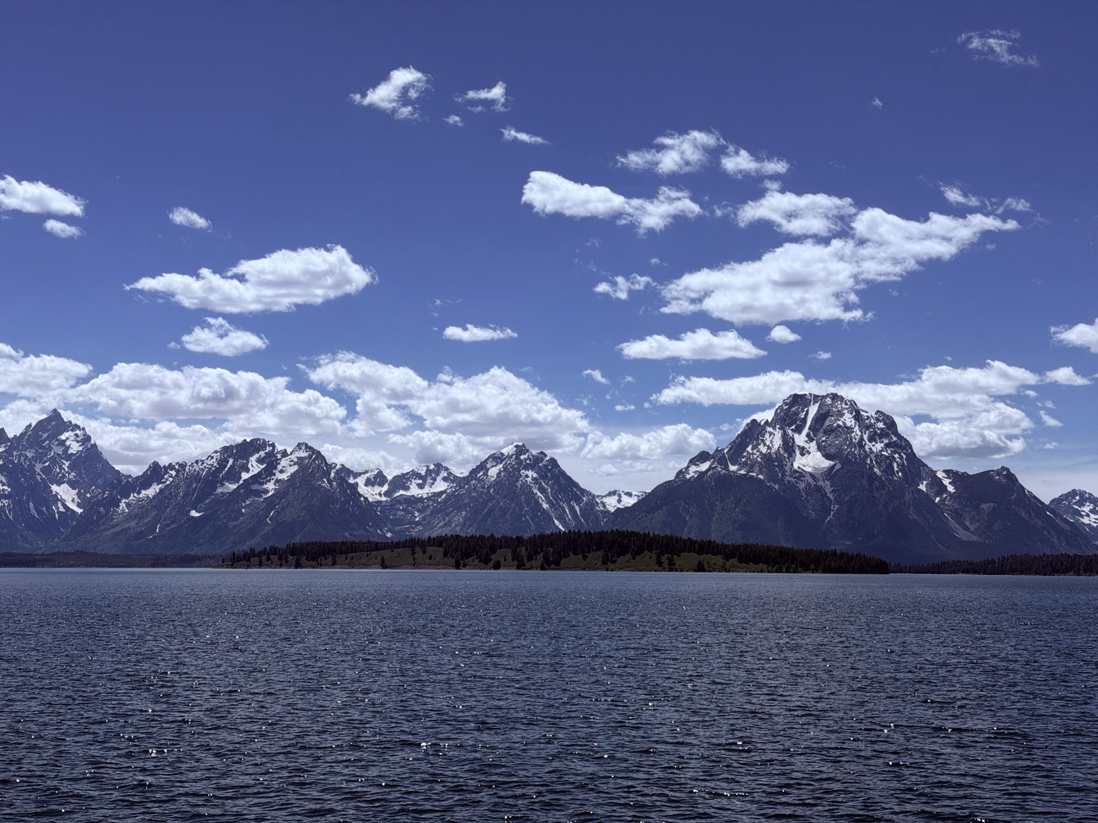 Jagged Teton peaks above a calm lake and forested shoreline