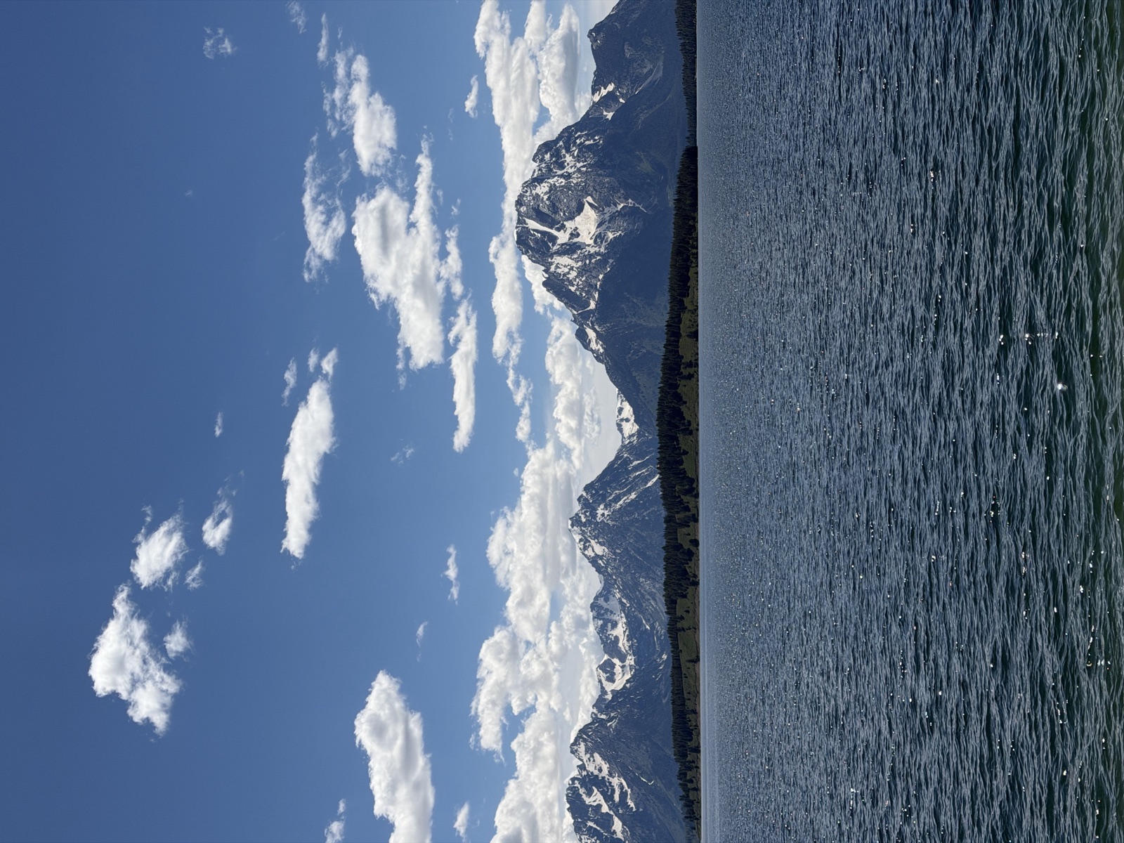 Teton peaks and forest reflected across a still blue lake