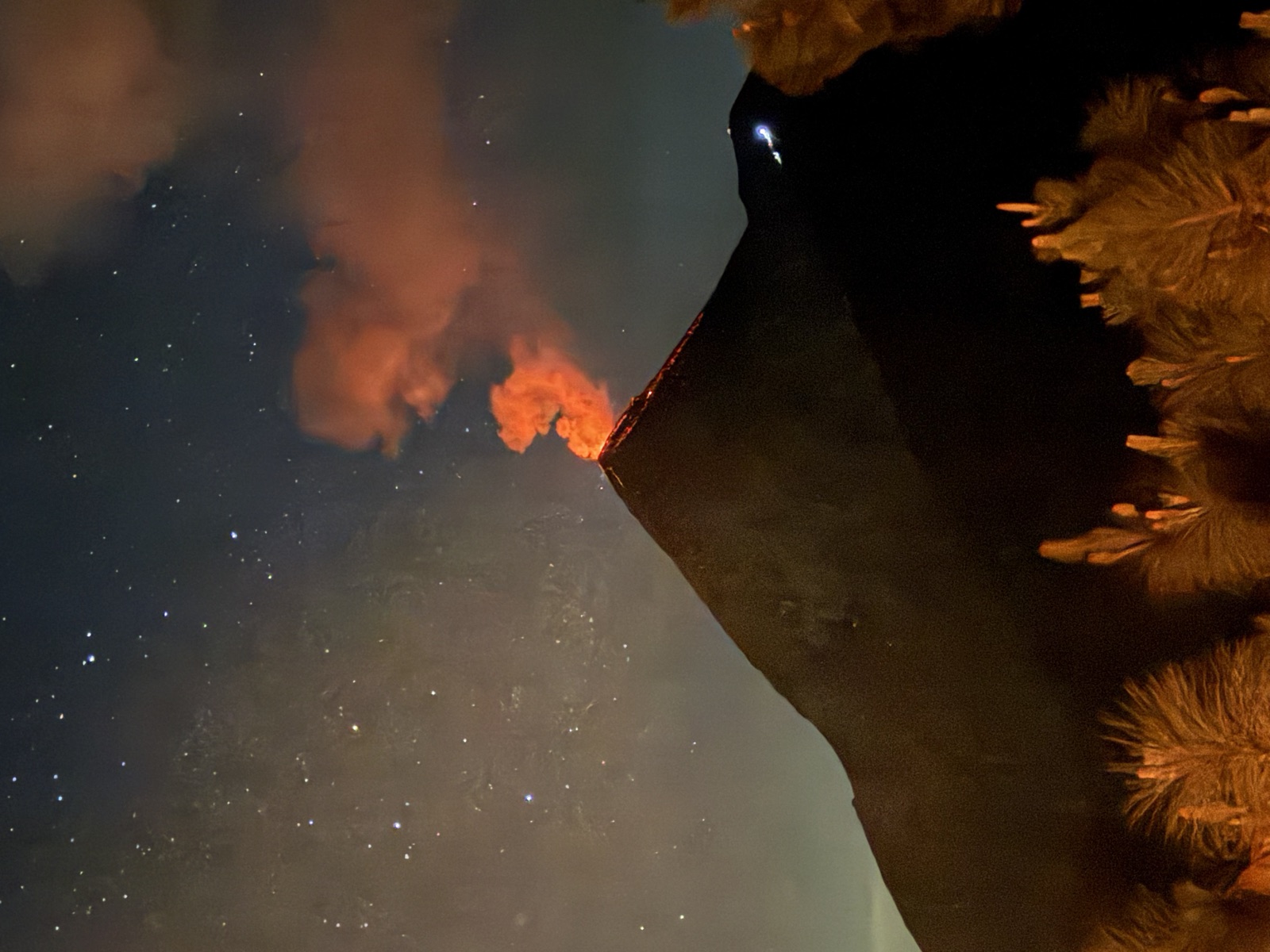 Fuego erupting orange under stars beyond dark pines