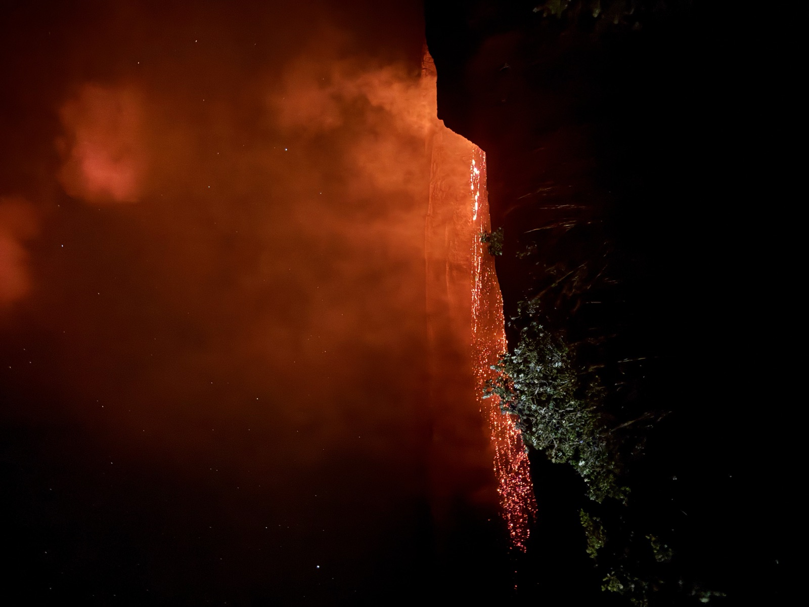 Orange lava glow rising from a volcanic crater at night