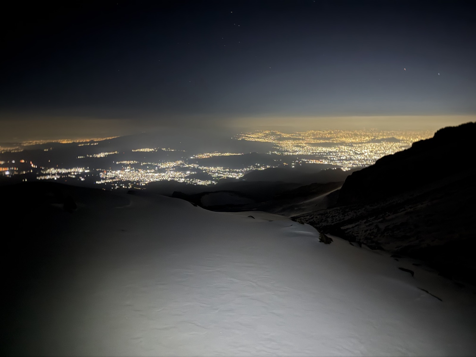 Snowy volcanic ledge above city lights at night